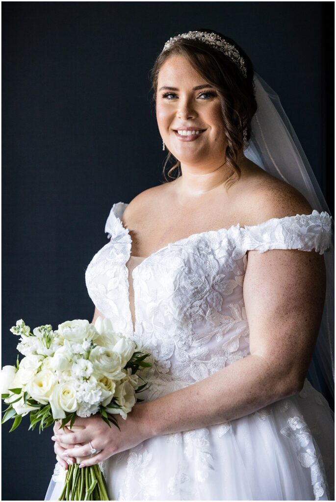 Bridal portrait with natural light - bride wears floral appliqué gown, headpiece and veil, and holds white and cream bouquet 