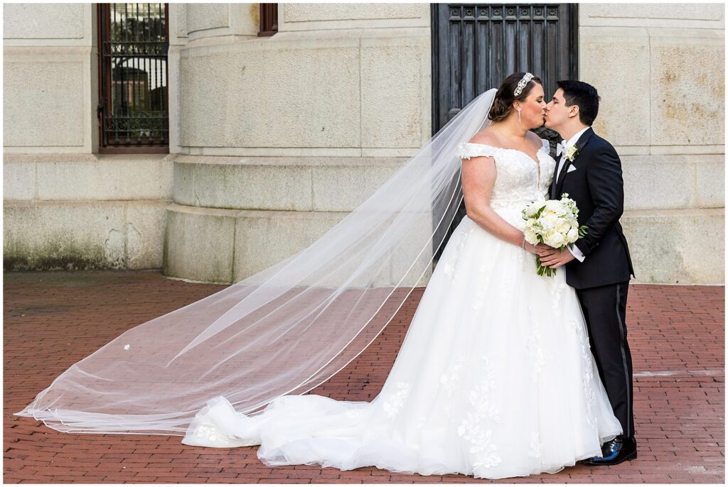 Bride and Groom share a kiss while Bride's veil floats behind her 