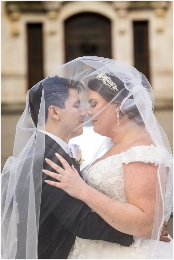 Bride and Groom embrace under her veil and touch noses slightly with their eyes closed