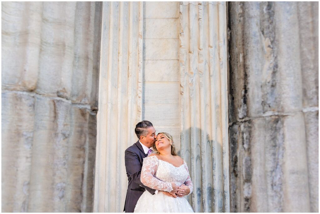 Newlyweds share an embrace and kiss near large marble columns