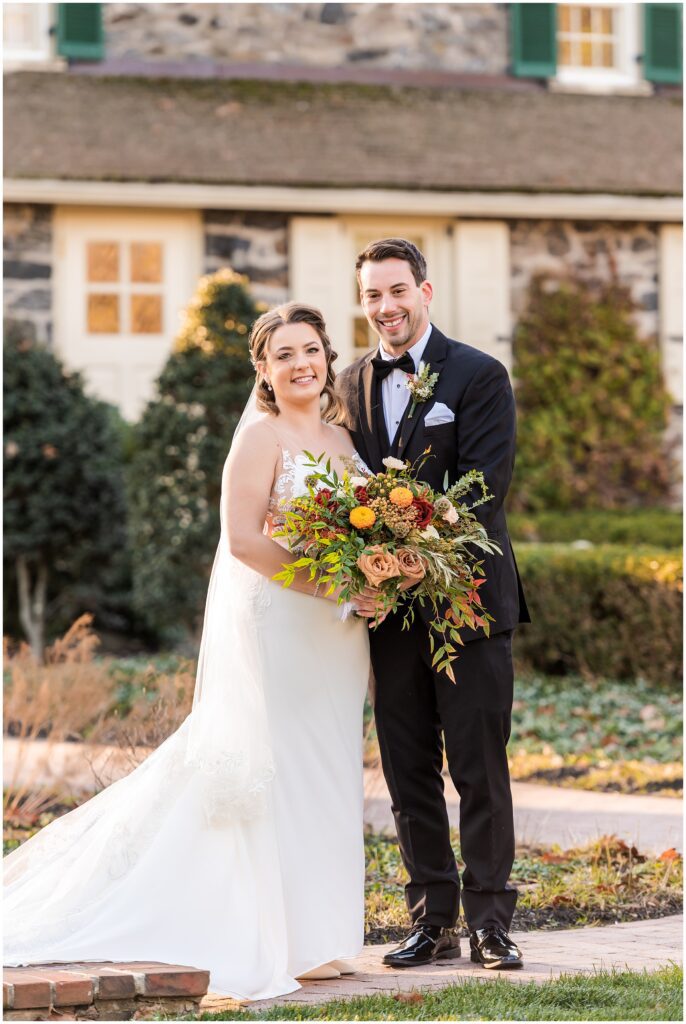 Bride holds her lush fall bouquet while standing with her Groom