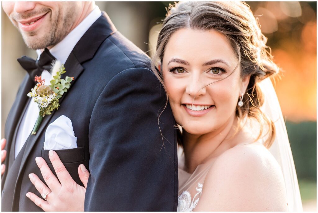 Bride looks directly at camera while embracing her groom from behind