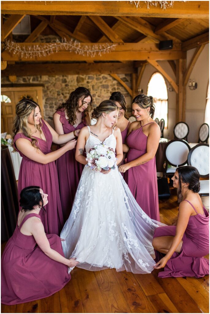 Wedding party in dark rose dresses surrounds bride holding white bouquet