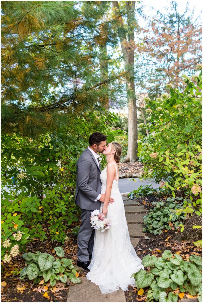 Newlyweds kiss in a lush green area at Meredith Manor