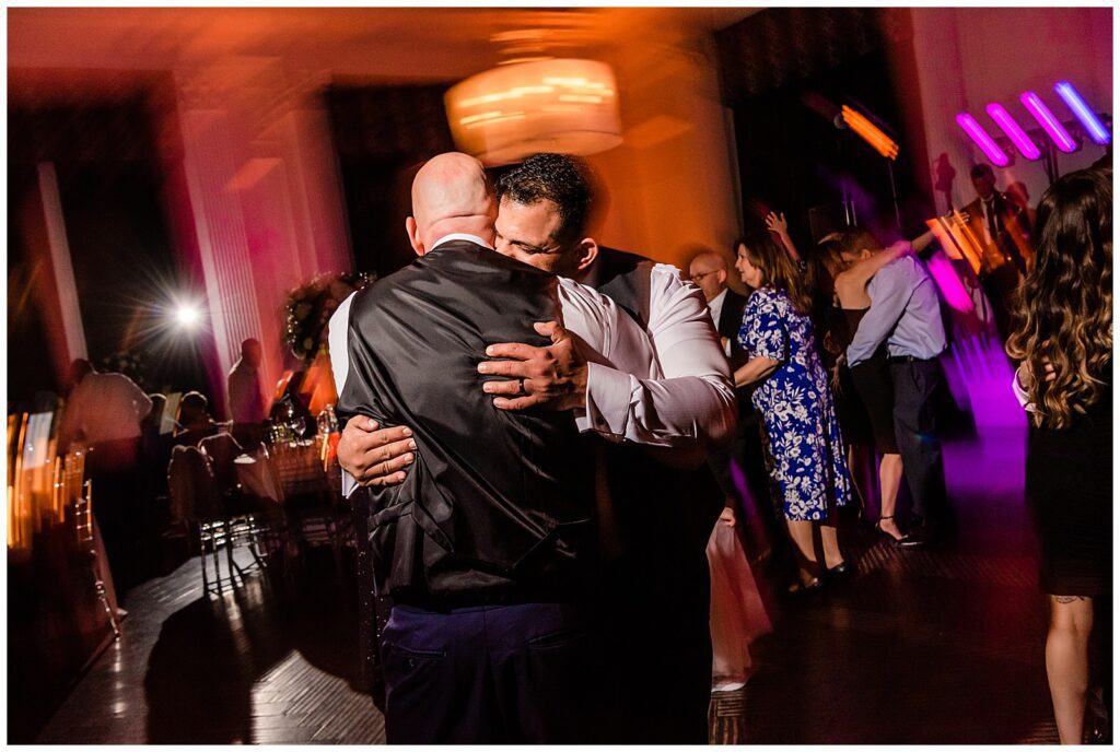 Grooms hugging on the dance floor with colored light blurs at Down Town Club reception | Ashley Gerrity Photography
