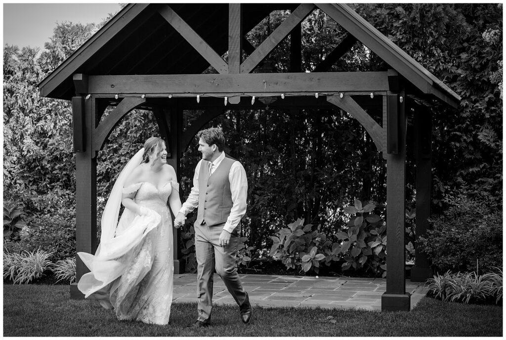 Black and white portrait of bride and groom holding hands and walking in outdoor courtyard at their Normandy Farm wedding | Ashley Gerrity Photography