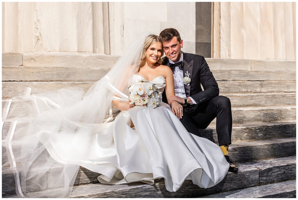 Bride and groom sitting on stone steps in front of the Second Bank in Old City Philadelphia before their Greek wedding at Union Trust | Ashley Gerrity Photography