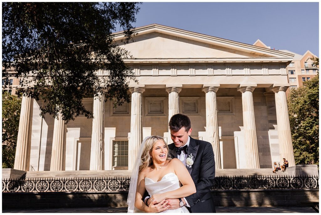 Bride and groom laughing while groom holds bride around her waist in front of the Second Bank in Philadelphia | Ashley Gerrity Photography