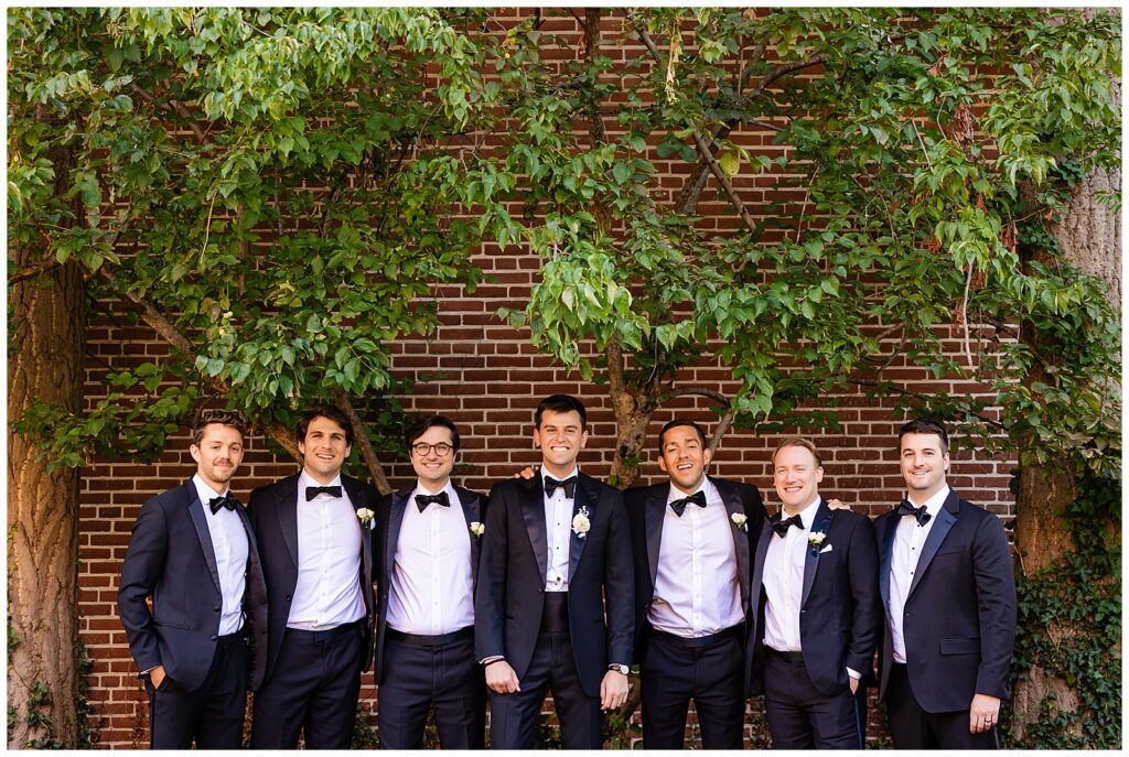 Traditional groomsmen portrait with grooms in black tuxedos in front of a brick wall and tree in Old City Philadelphia | Ashley Gerrity Photography