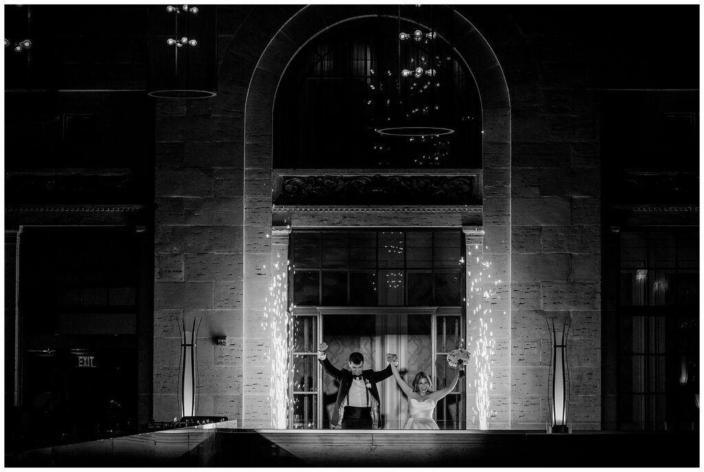 Black and white portrait of bride and groom cheering with their hands up as sparklers go off next to them during their entrance to Union Trust wedding reception | Ashley Gerrity Photography