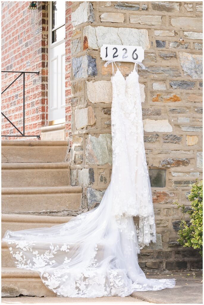 Lace wedding gown with long train hanging from address sign against stone wall | Ashley Gerrity Photography