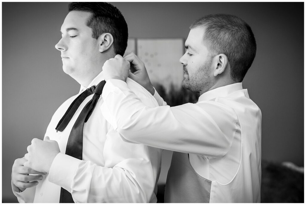 Black and white portrait of best man helping groom put on his tie | Ashley Gerrity Photography