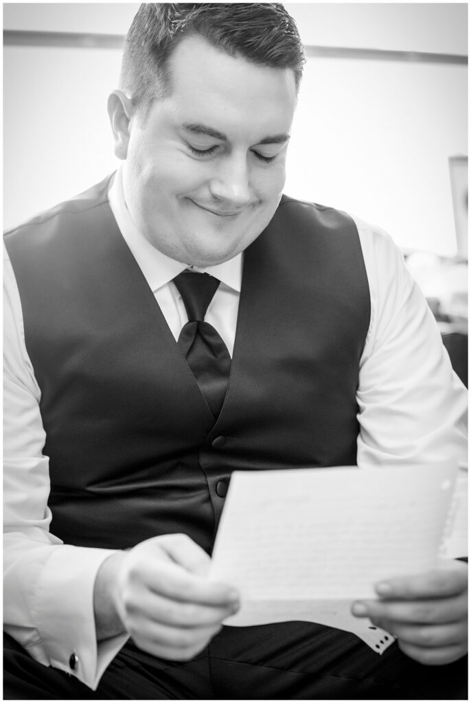 Black and white portrait of groom reading handwritten letter from bride before their church wedding ceremony | Ashley Gerrity Photography