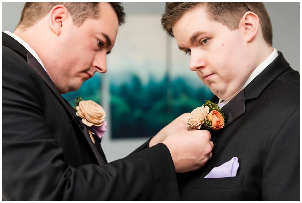 Groom pinning wooden floral boutonniere on his brother | Ashley Gerrity Photography
