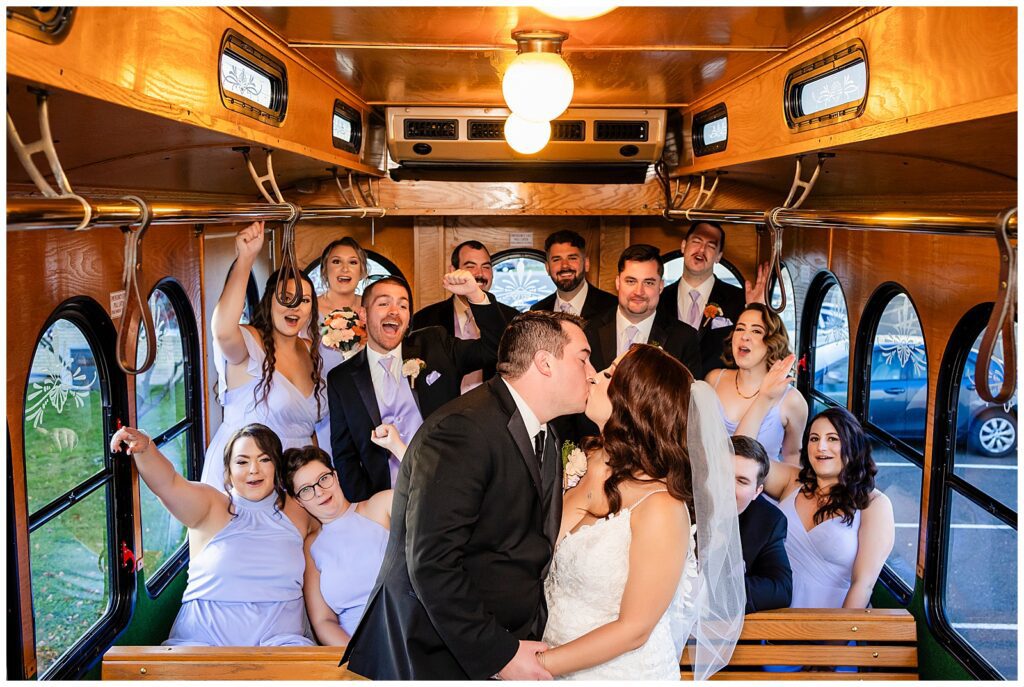 Bride and groom stand and kiss in front of cheering wedding party on their wedding trolley | Ashley Gerrity Photography