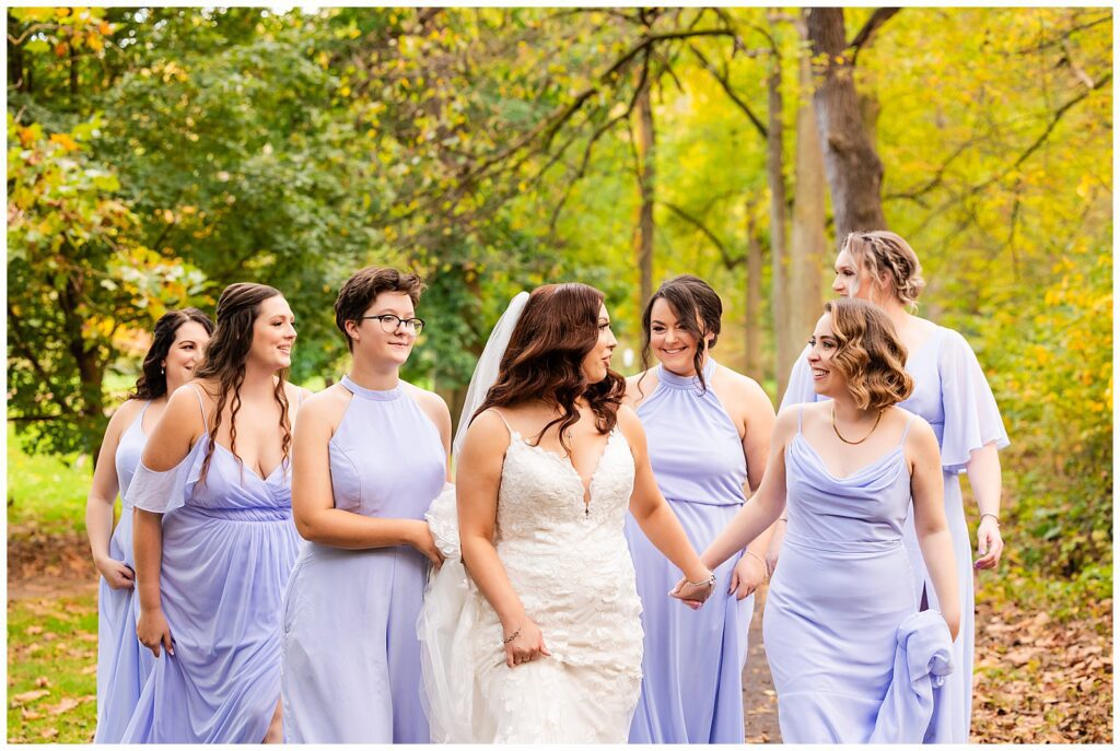 Bride holding hands with bridesmaids as they walk down park path at Pennypack Park | Ashley Gerrity Photography