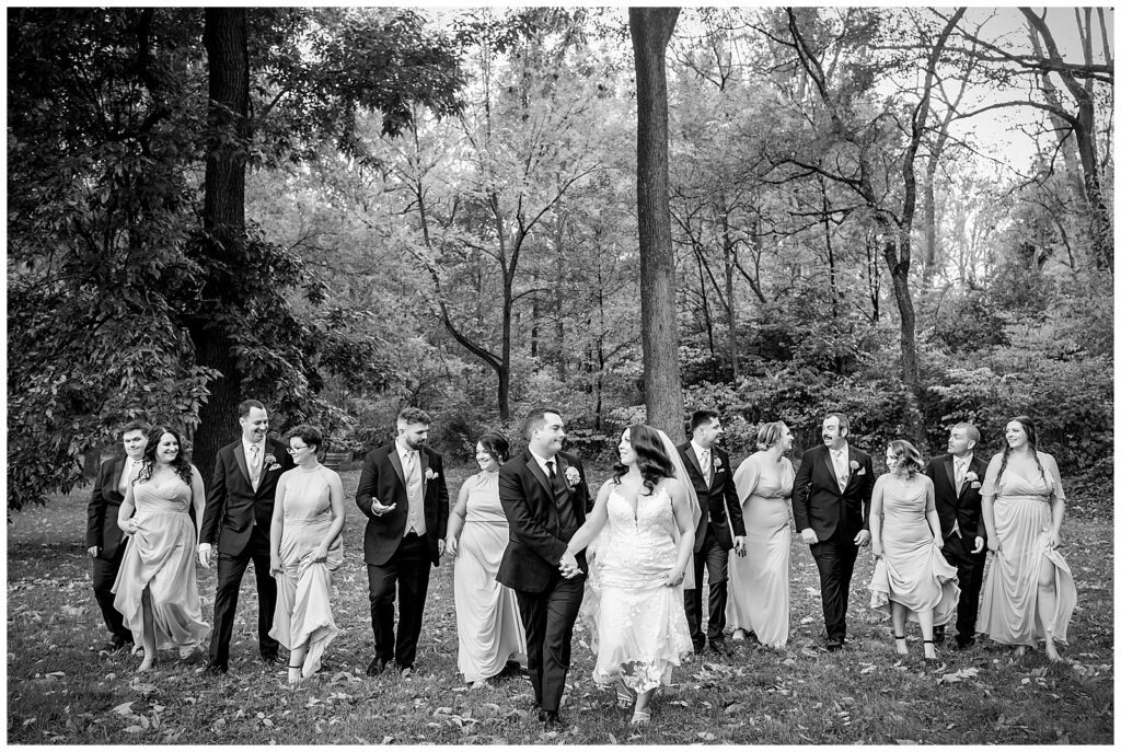 Black and white wedding party portrait of bridesmaids and groomsmen walking through field with bride and groom at Pennypack Park | Ashley Gerrity Photography