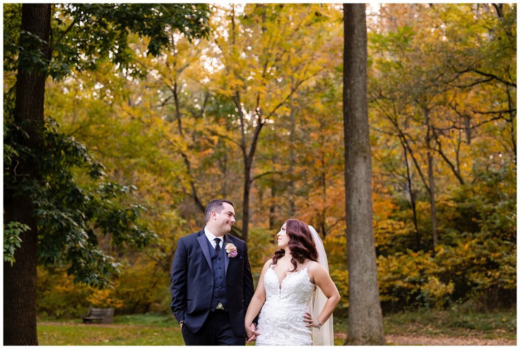 Pennypack Park wedding portrait of bride and groom holding hands and looking at each other in front of Fall foliage | Ashley Gerrity Photography