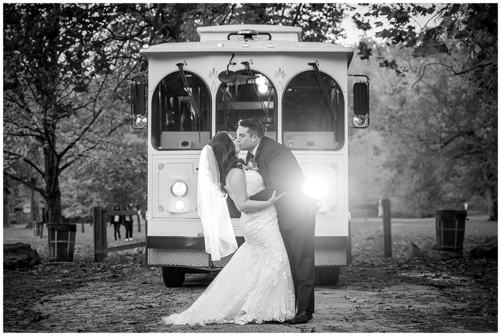 Black and white portrait of groom dipping and kissing bride in front of classic Philadelphia wedding trolley in Pennypack Park | Ashley Gerrity Photography