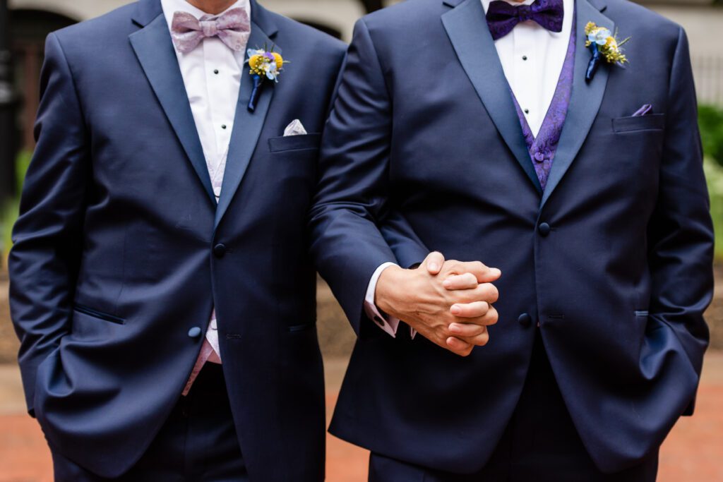 Torso Crop of two grooms in blue suits with bow ties holding hands
