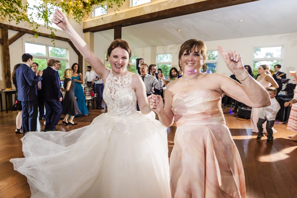 Bride in a lacey wedding dress & her mother in pink dancing a fast dance together